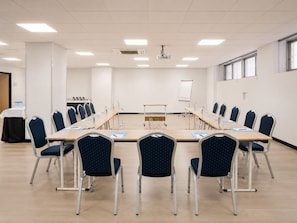Un salón de conferencias con una mesa larga, sillas, un proyector y una pizarra.