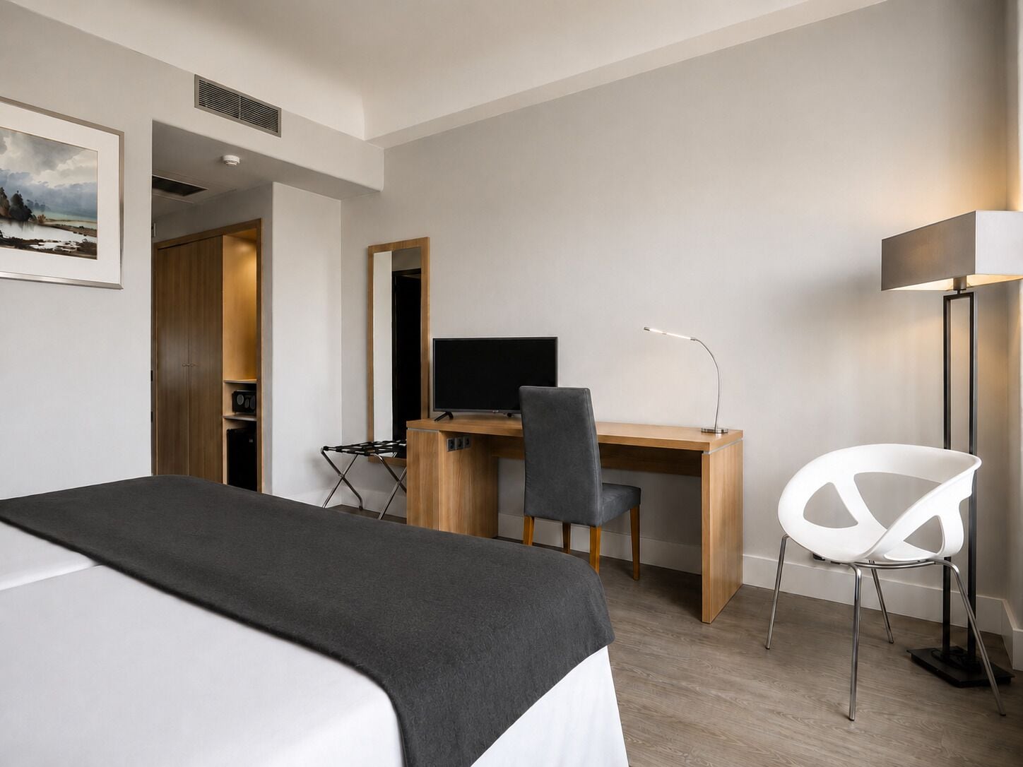 Une chambre d’hôtel avec un lit, un bureau équipé d’un ordinateur, une chaise, une lampe et un grand miroir.