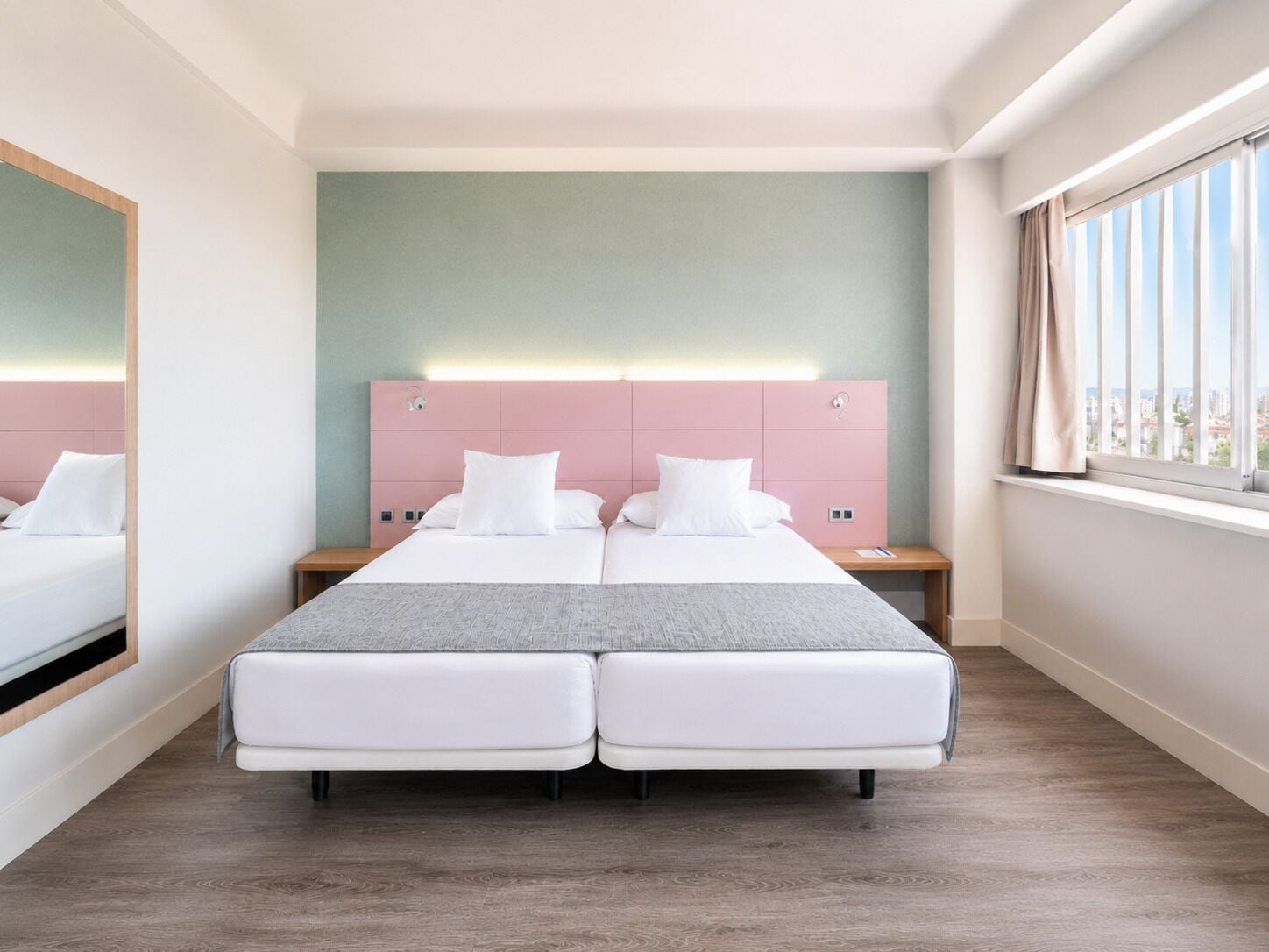 A double bed with a pink headboard, a bedside table, and a window with curtains.