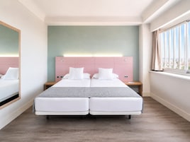 Ein Doppelbett mit rosa Kopfteil, ein Nachttisch und ein Fenster mit Vorhängen.