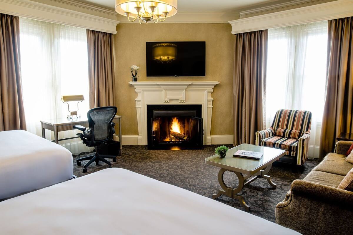 Une chambre d’hôtel avec une cheminée, une télévision, un lit, un bureau et un fauteuil à rayures.