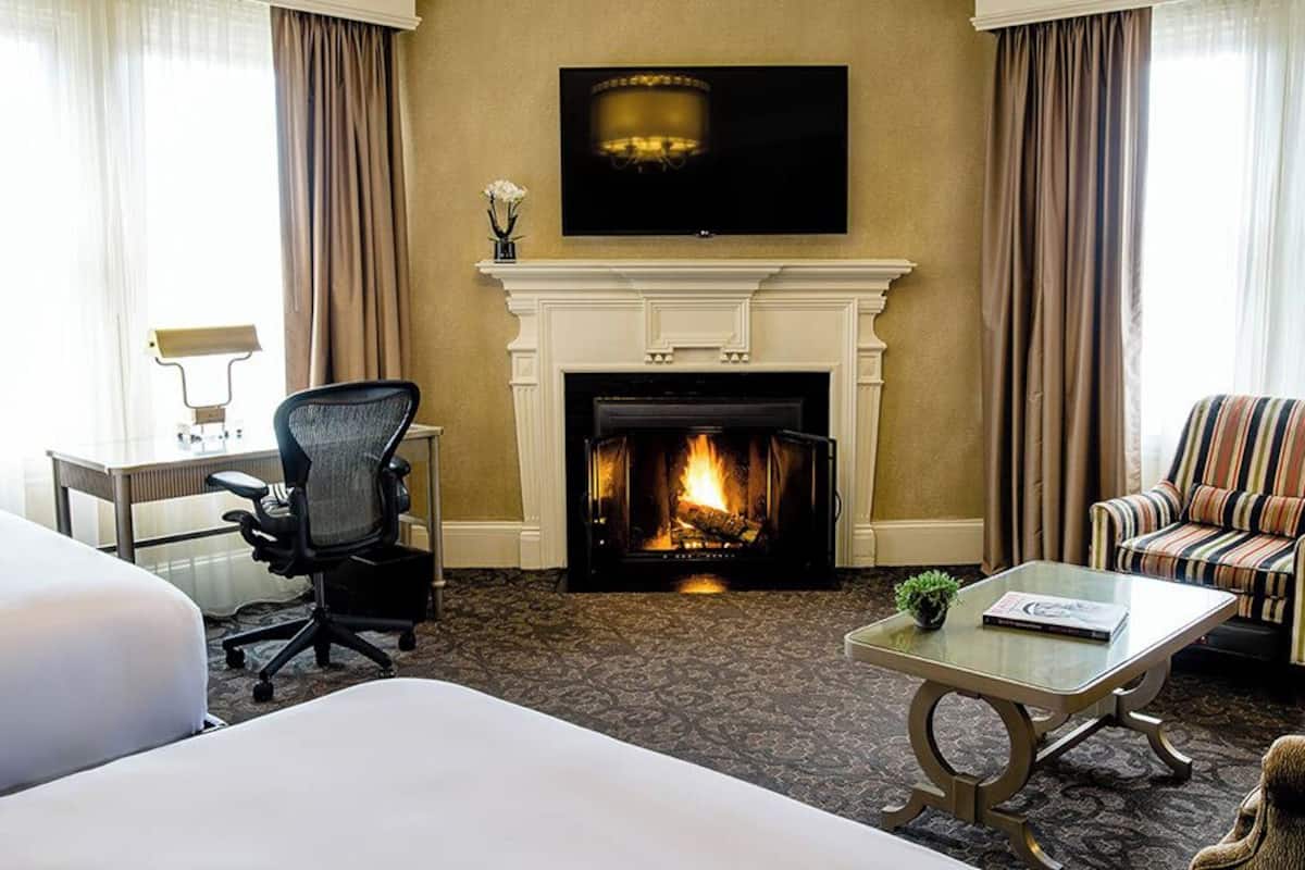 Une chambre d’hôtel avec une cheminée, un lit, un bureau, une chaise et un canapé.