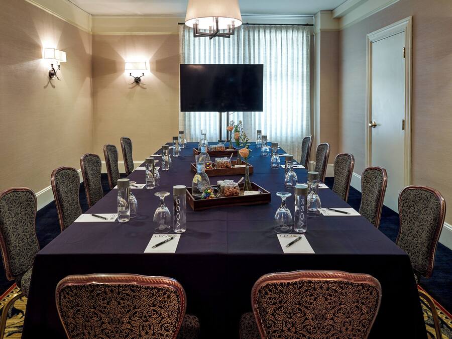 Une salle de conférence avec une longue table, des chaises, un téléviseur à écran plat et des appliques murales.