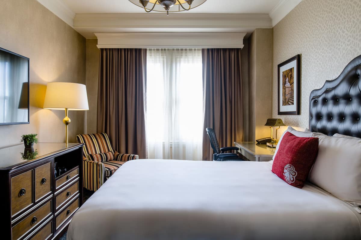 Une chambre d’hôtel avec un grand lit, un bureau avec une lampe, une chaise et un téléviseur.
