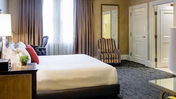 Una habitación de hotel con una cama, un escritorio con lámpara, una silla y una puerta.
