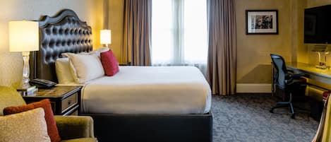 A hotel room with a large bed, a desk with a chair, a sofa, and a television.