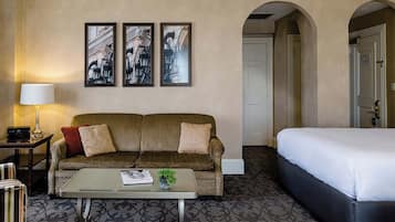 A hotel room with a sofa, a bed, a coffee table, and framed pictures on the wall.
