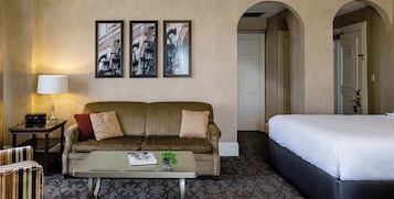 A hotel room with a sofa, a bed, a coffee table, and framed pictures on the wall.