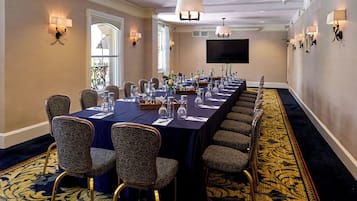 A conference room with a long table, patterned chairs, and wall-mounted lighting.