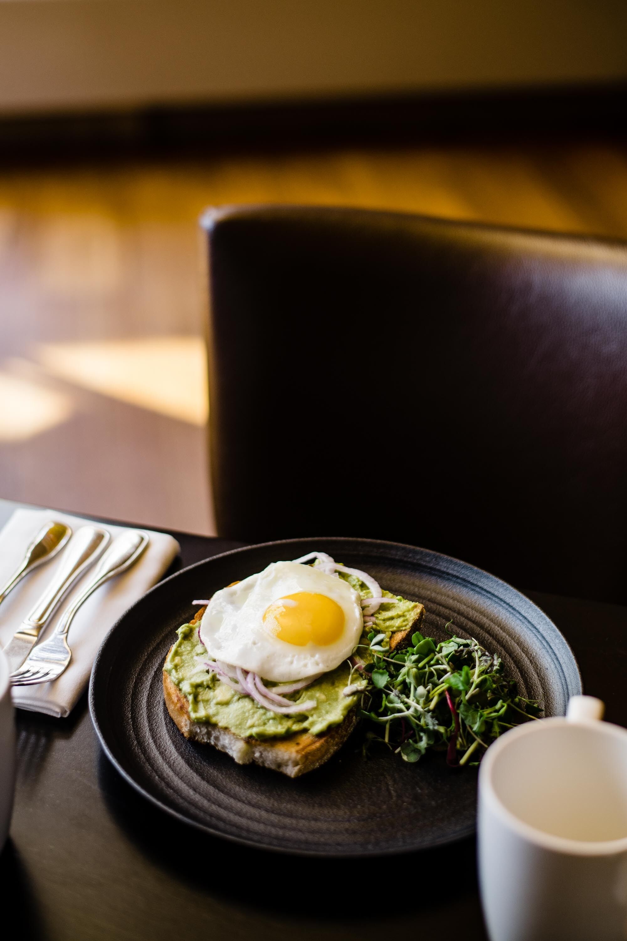 Une assiette avec un sandwich, une tasse et des couverts sur une table.