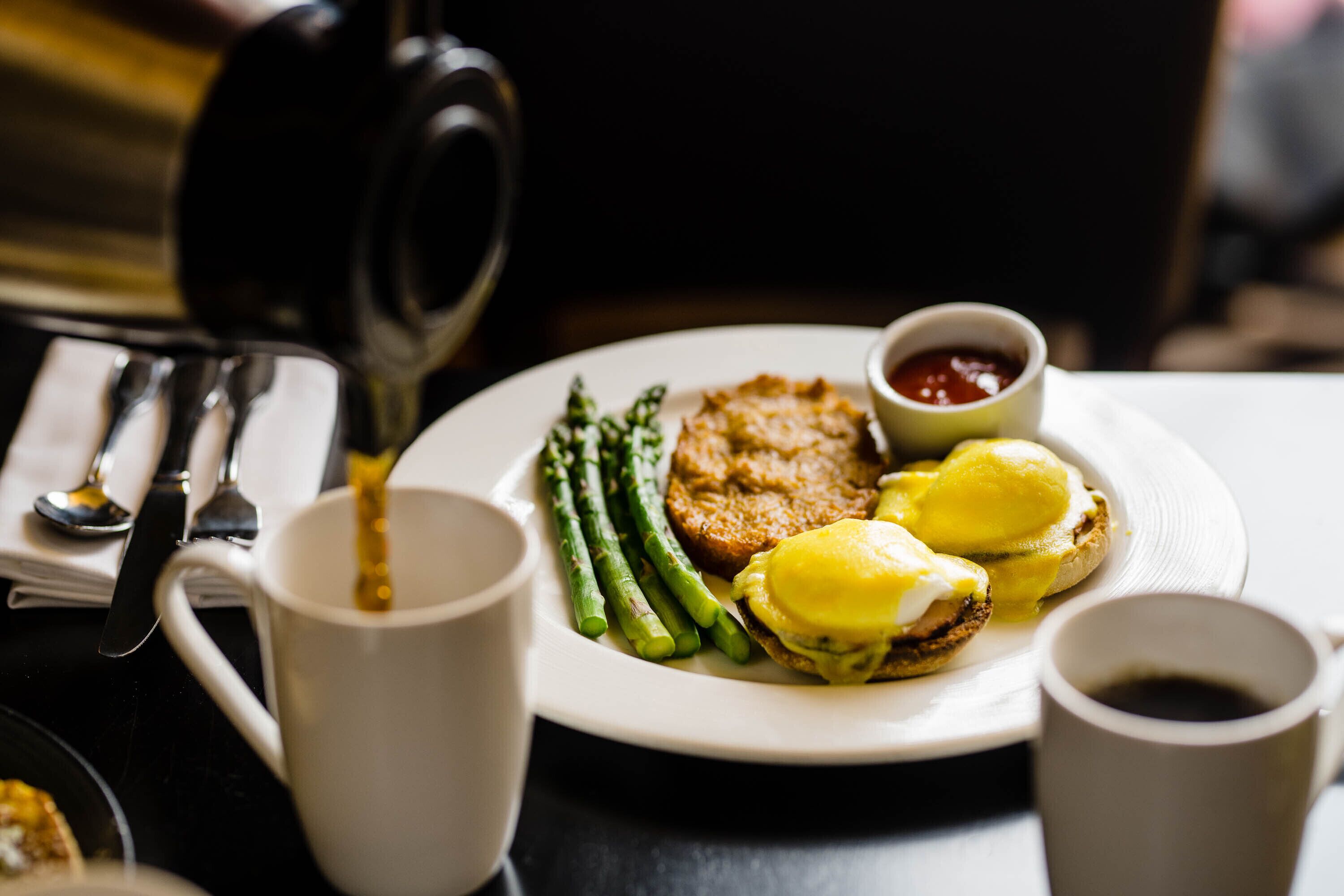 A plate with eggs benedict, asparagus, and a small bowl of ketchup.