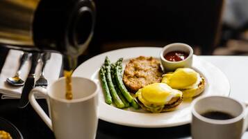 A plate with eggs benedict, asparagus, and a small bowl of ketchup.