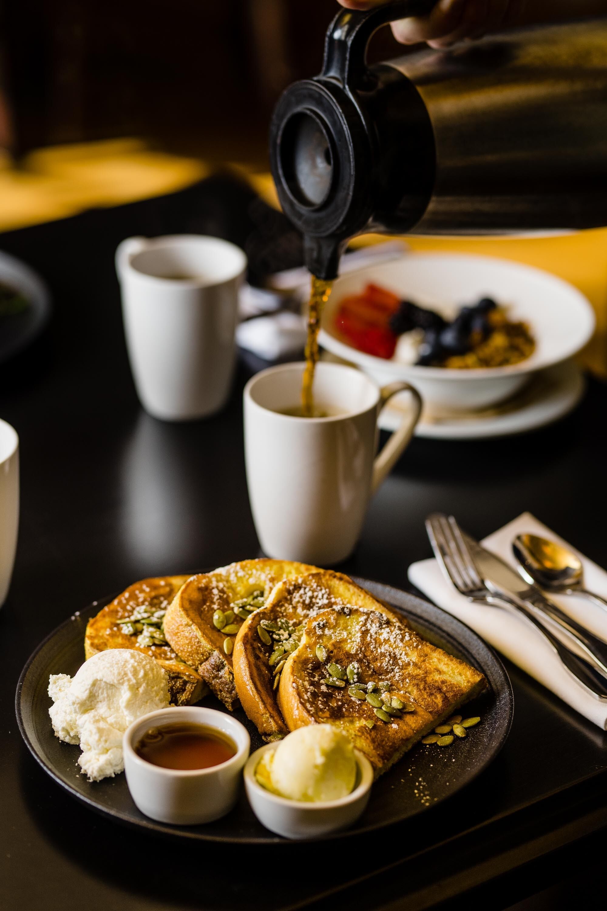 A breakfast setting with pancakes, butter, syrup, and a cup of coffee on a table.