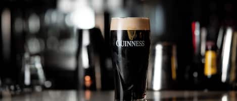 A glass of Guinness beer on a bar counter with a blurred background of bottles.