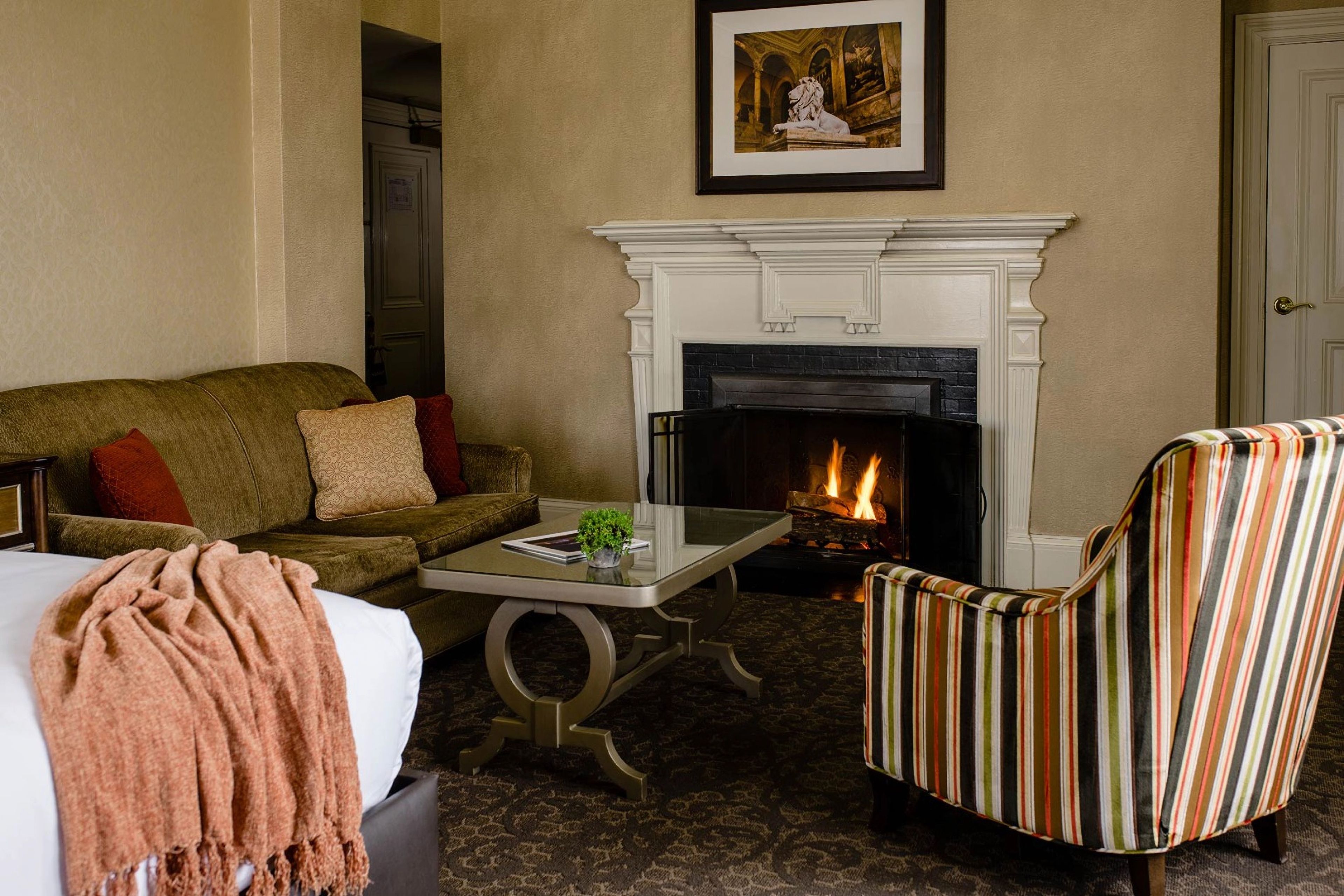 A cozy living room with a fireplace, a sofa, a striped armchair, and a coffee table.