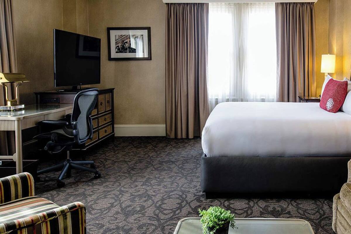 Une chambre d’hôtel avec un grand lit, un bureau avec une chaise, une télévision et une petite table avec une plante.