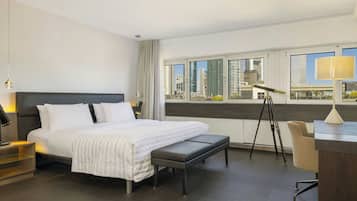 A modern hotel room with a large bed, a desk, and a view of the cityscape.