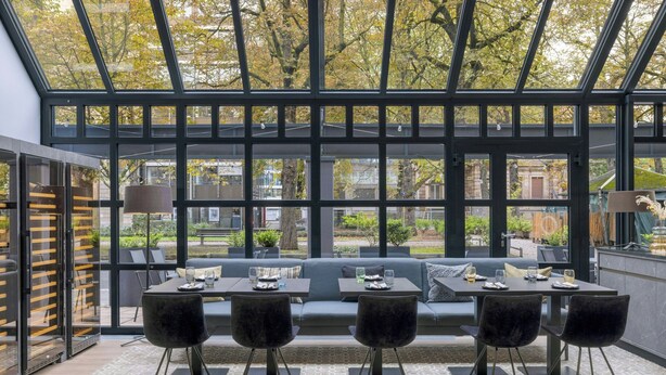 A modern outdoor seating area with a glass enclosure, a sofa, and a table with chairs. - Le Méridien Frankfurt (Frankfurt)