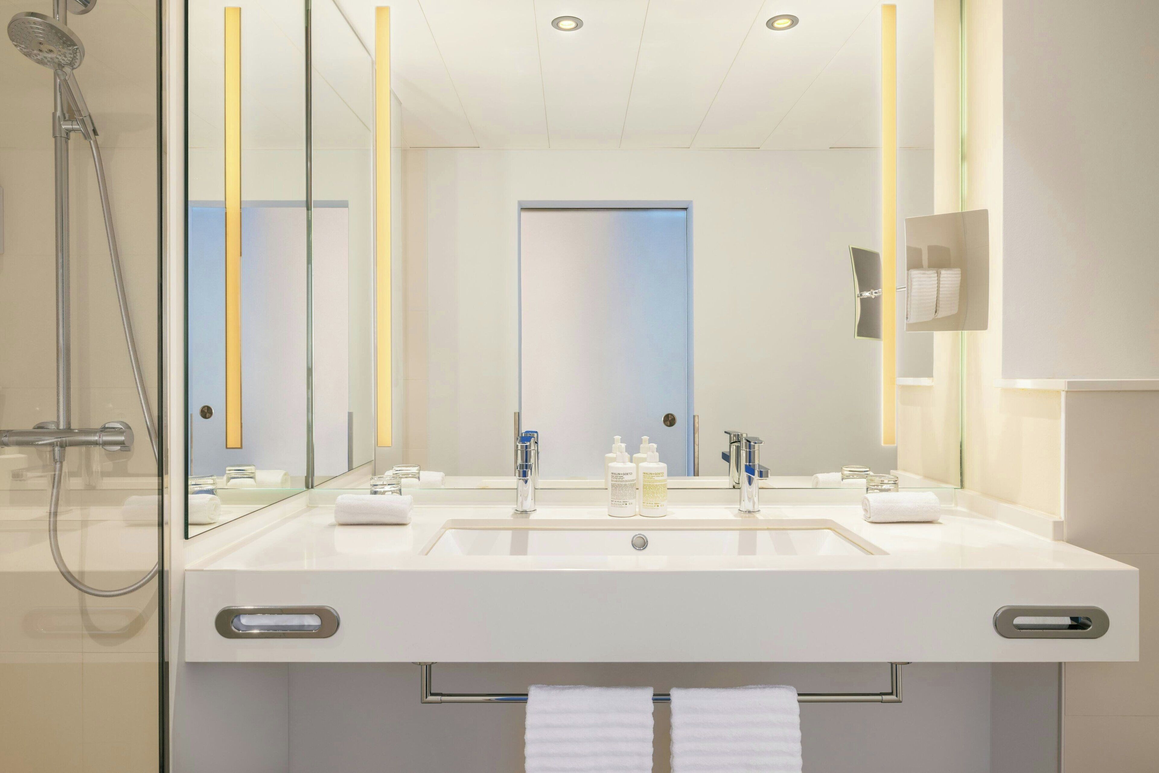 A modern bathroom with a glass-enclosed shower, a double sink with a mirror above, and a towel rack with two towels.