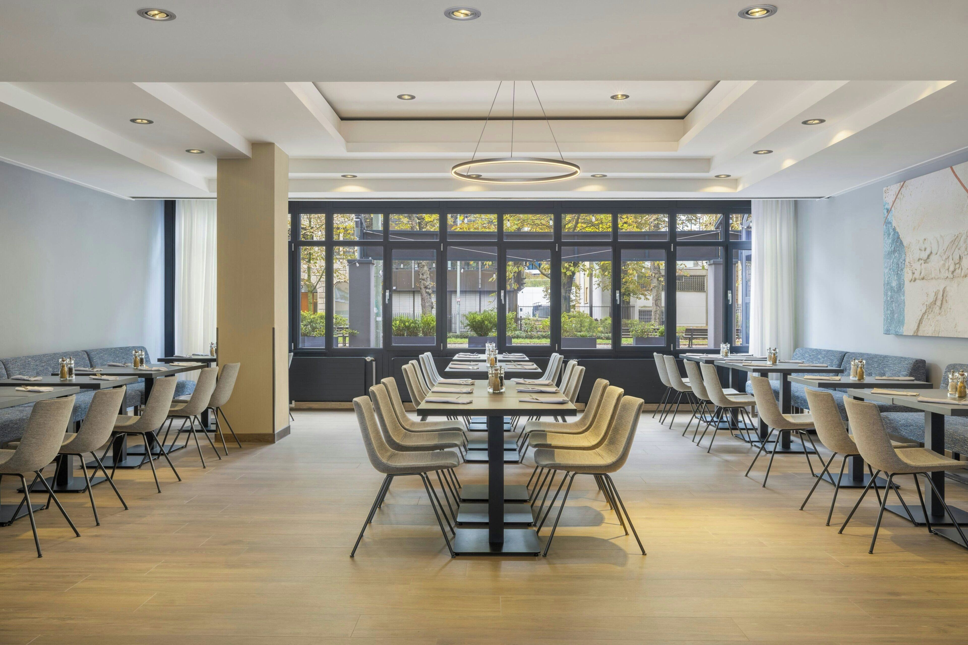 A modern dining area with long tables and chairs, large windows with a view of the outside, and a clean, minimalist design.