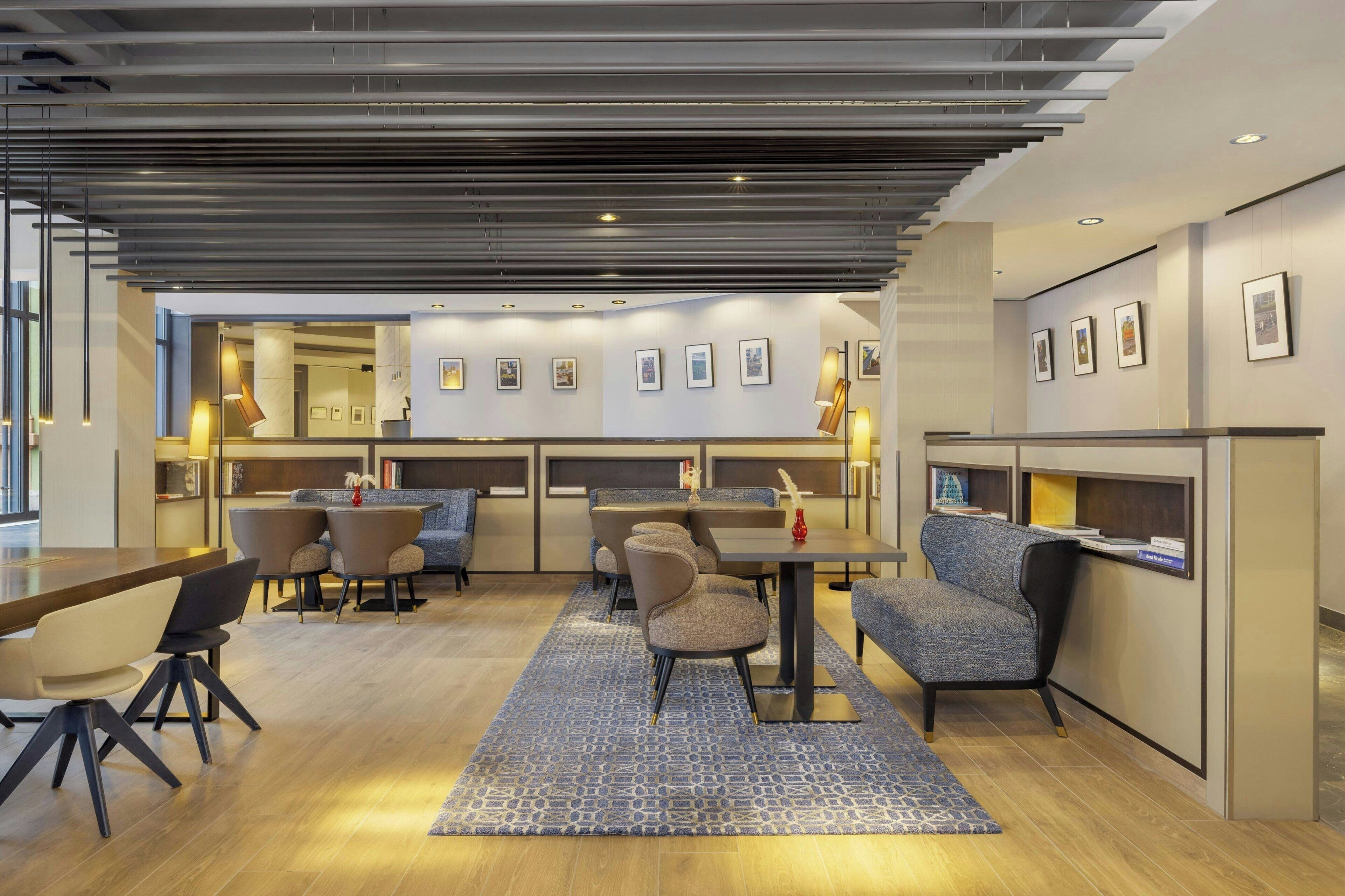A modern hotel lobby with a central seating area, a reception desk, and framed artwork on the walls.