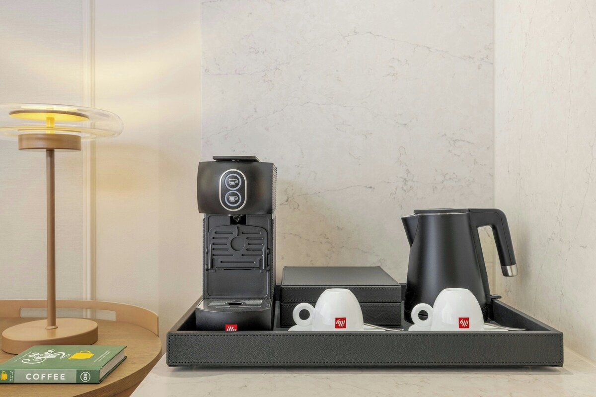 A modern coffee station with a coffee machine, two cups, and a kettle on a tray.