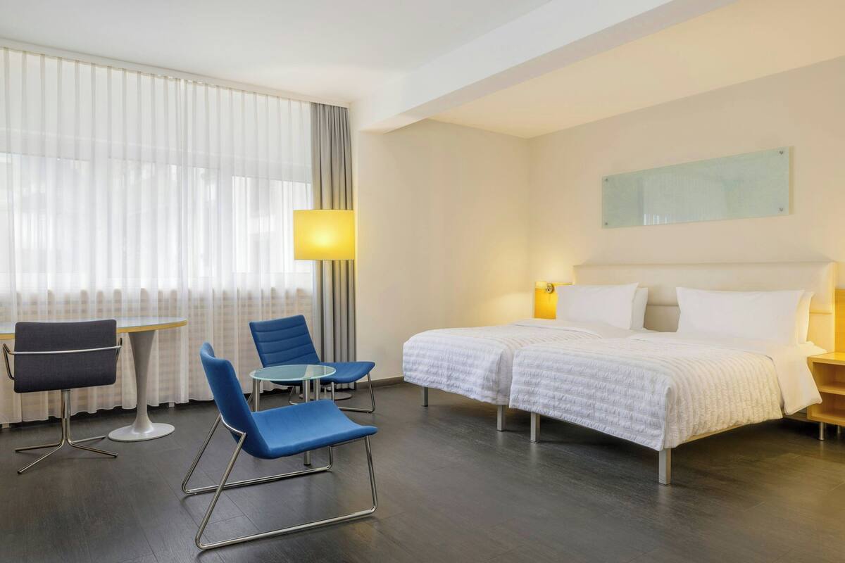 A hotel room with a bed, two chairs, a small table, and a lamp.