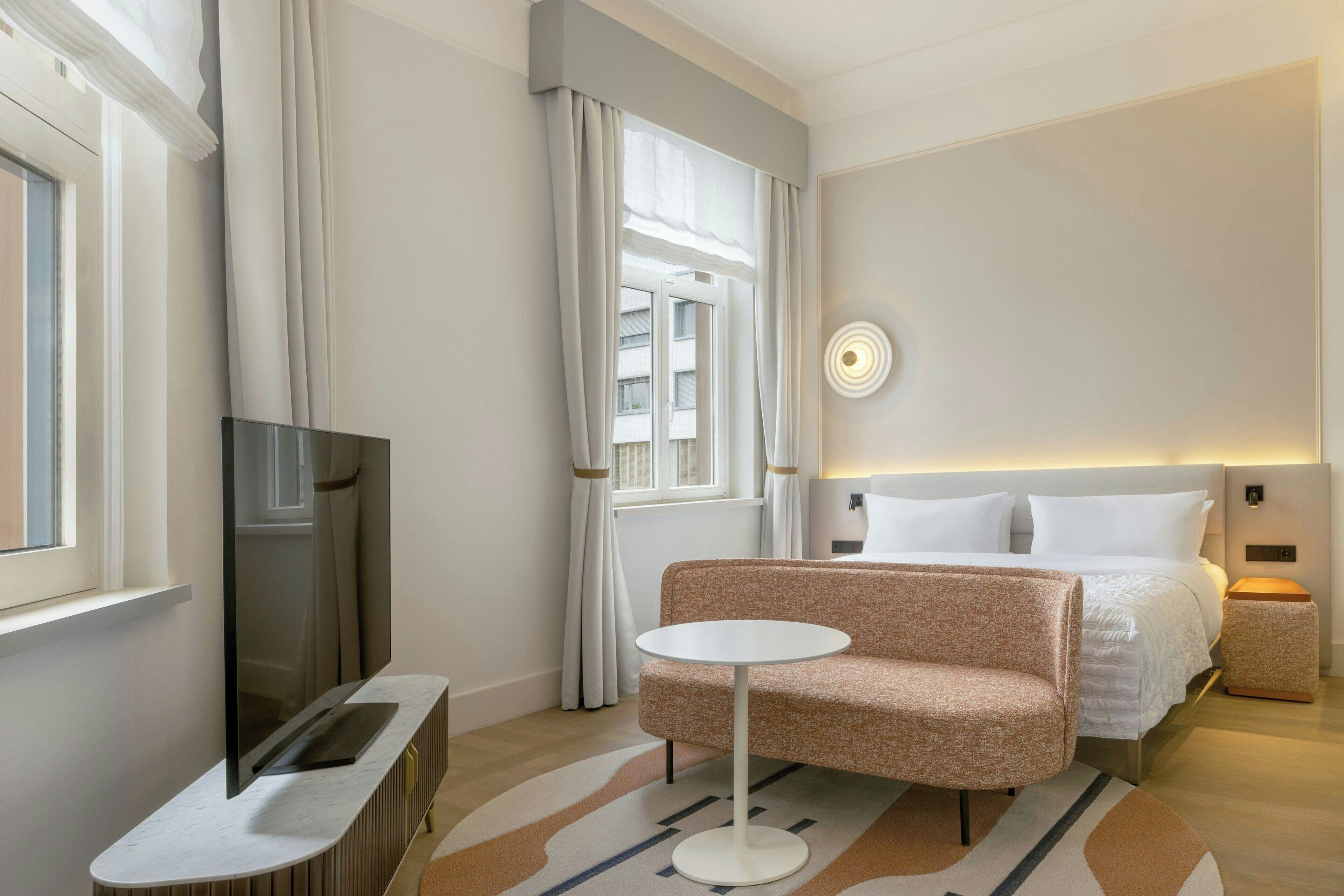Una habitación de hotel moderna con una cama, un sofá, un televisor y una mesita.