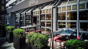 An outdoor seating area with tables and chairs, a building with a sign reading "The Legacy," and potted plants. - Le Méridien Frankfurt (Frankfurt)