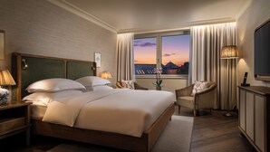 A hotel room with a large bed, a sitting area with a chair, a desk, and a TV.