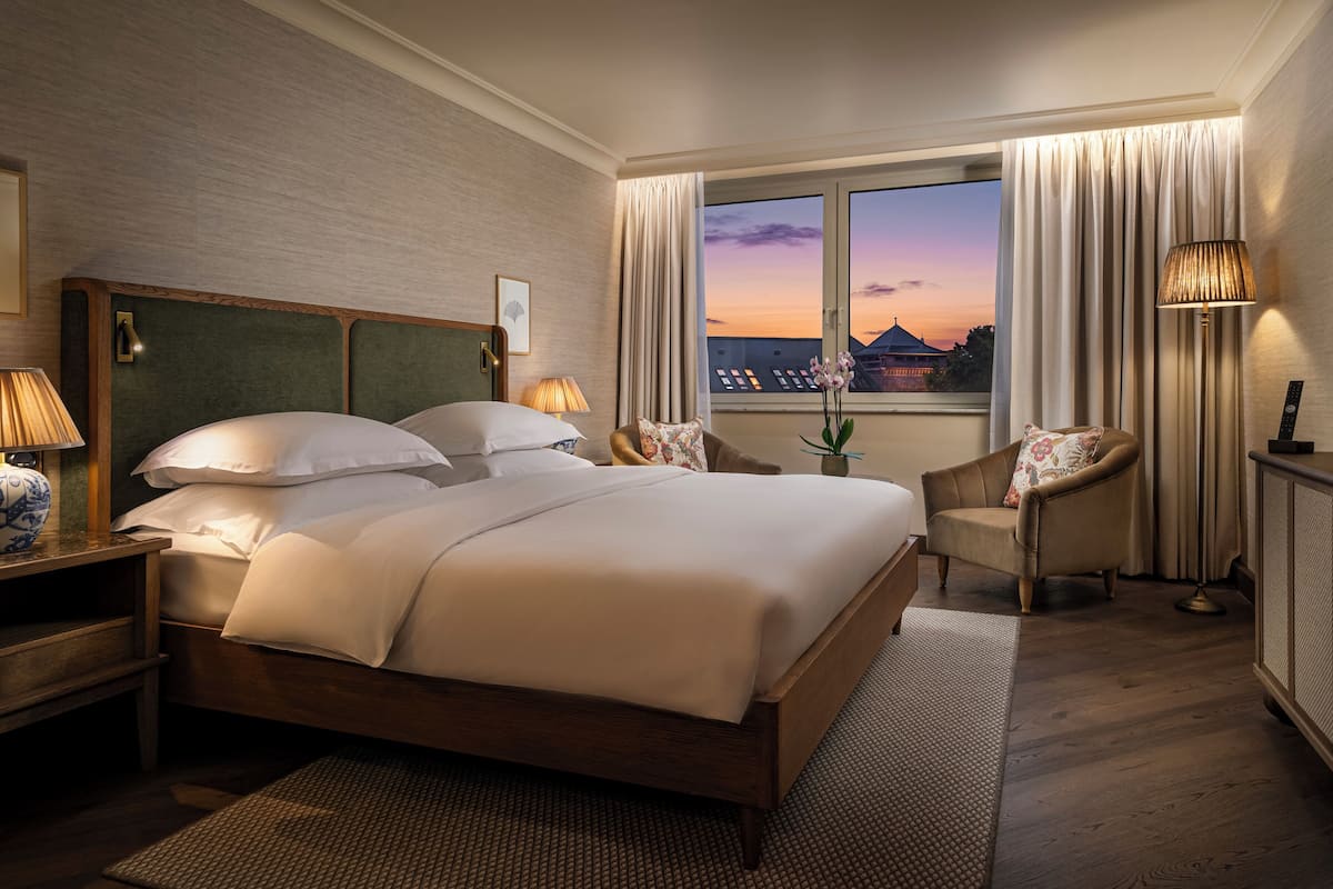 Una habitación de hotel con una cama grande, una zona de estar con una silla, un escritorio y un televisor.