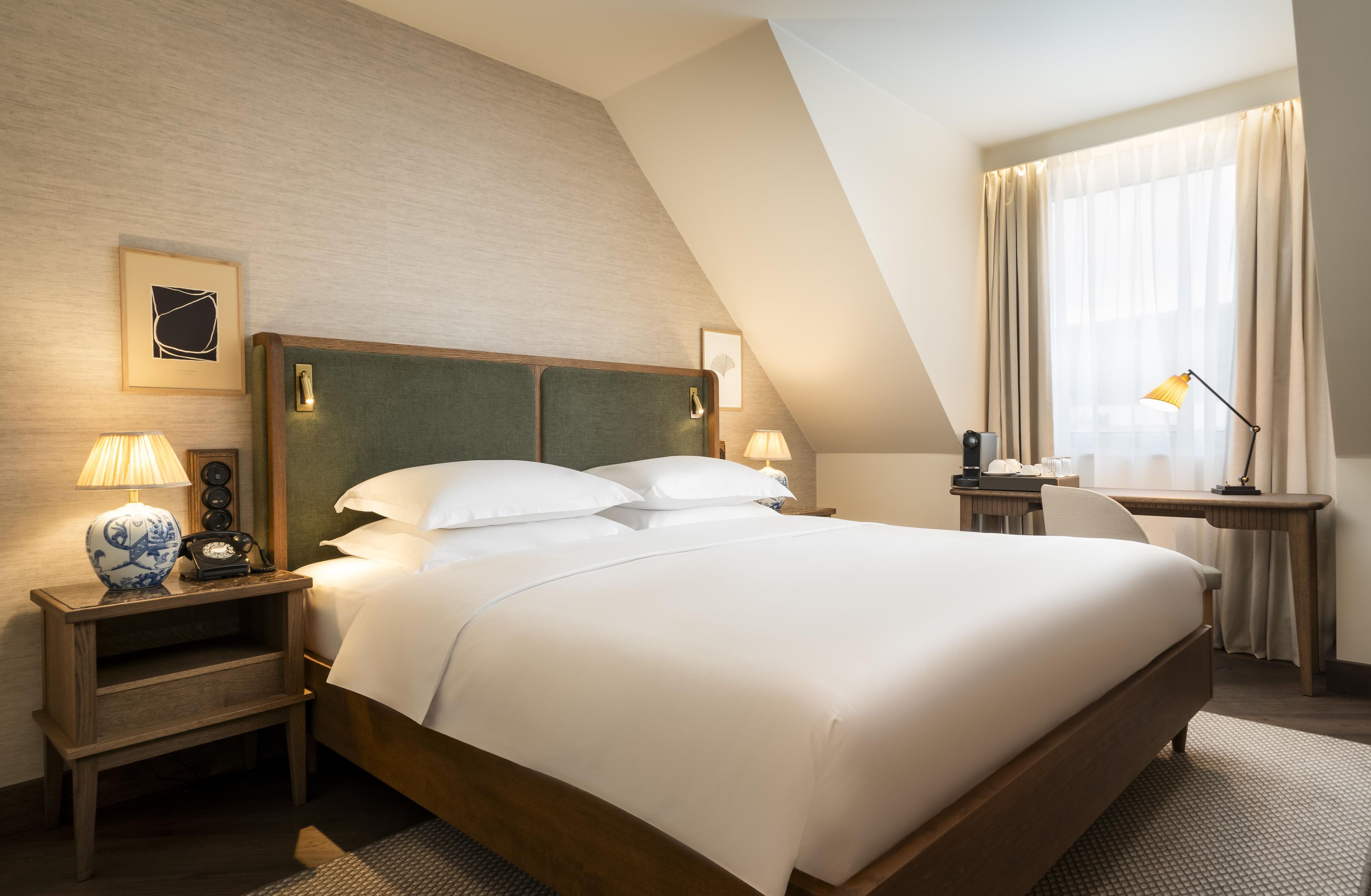 Une chambre d’hôtel avec un grand lit, des tables de chevet, des lampes, un bureau et une fenêtre avec des rideaux.
