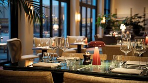A restaurant setting with tables set for dining, featuring wine glasses, cutlery, and a candle centerpiece.