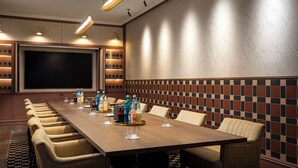 A conference room with a long table, chairs, and a large screen.