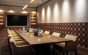 A conference room with a long table, chairs, and a large screen.