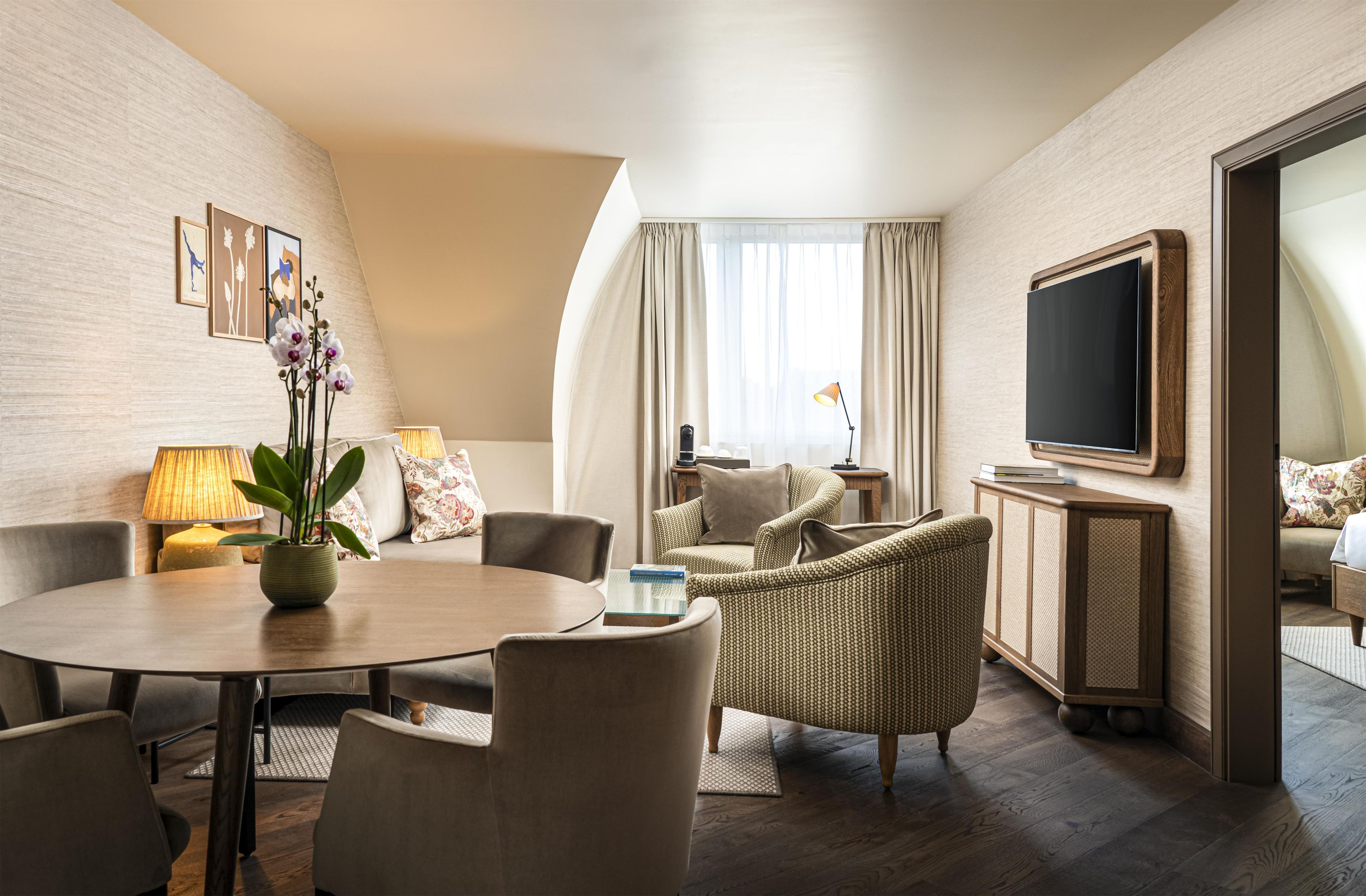 A hotel room with a round dining table, two sofas, a TV, and a large window with curtains.