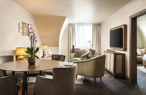 A hotel room with a round dining table, two sofas, a TV, and a large window with curtains. - Brunfels Hotel, in the Unbound Collection by Hyatt (Mainz)