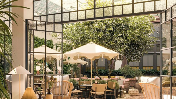 An indoor patio area with wicker furniture, umbrellas, and a view of greenery through large windows.