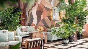 A cozy indoor seating area with a sofa, chairs, and a coffee table, surrounded by potted plants and a patterned wall.