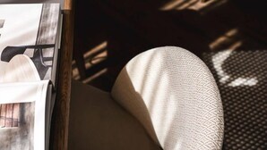 A close-up of a room corner with a wooden side table, a magazine, and a patterned cushion.
