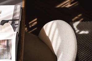 A close-up of a room corner with a wooden side table, a magazine, and a patterned cushion.