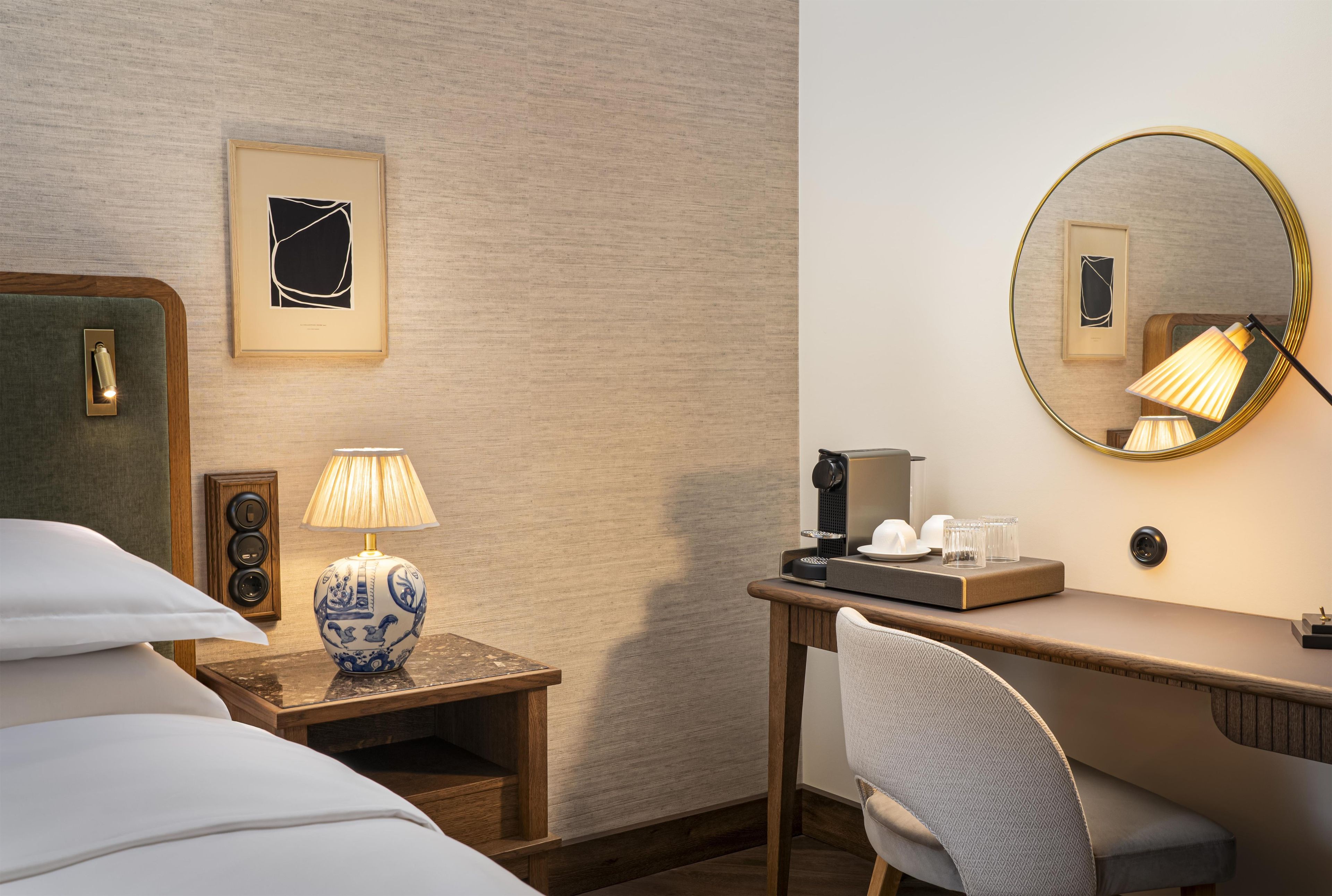 Ein Hotelzimmer mit einem Bett, einem Schreibtisch mit Lampe, einer Kaffeemaschine und einem Spiegel.