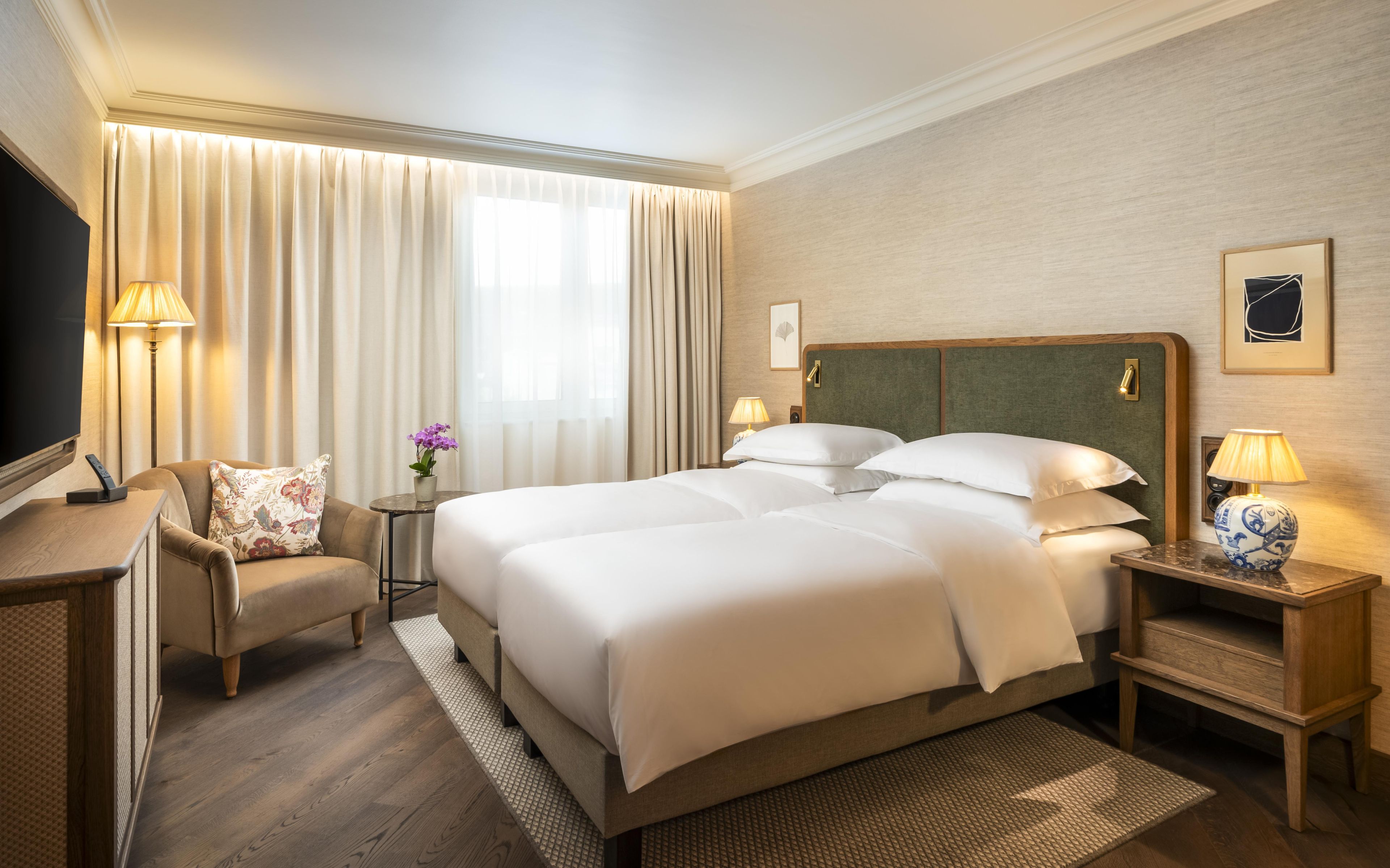 A hotel room with a large bed, a desk, a chair, and a television.