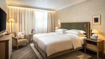 A hotel room with a large bed, a desk, a chair, and a television.