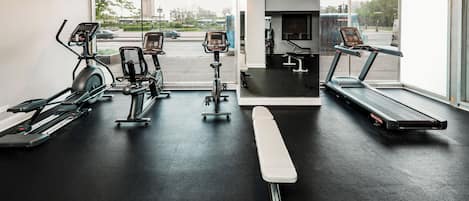 A gym with various exercise equipment including treadmills, stationary bikes, and a bench.