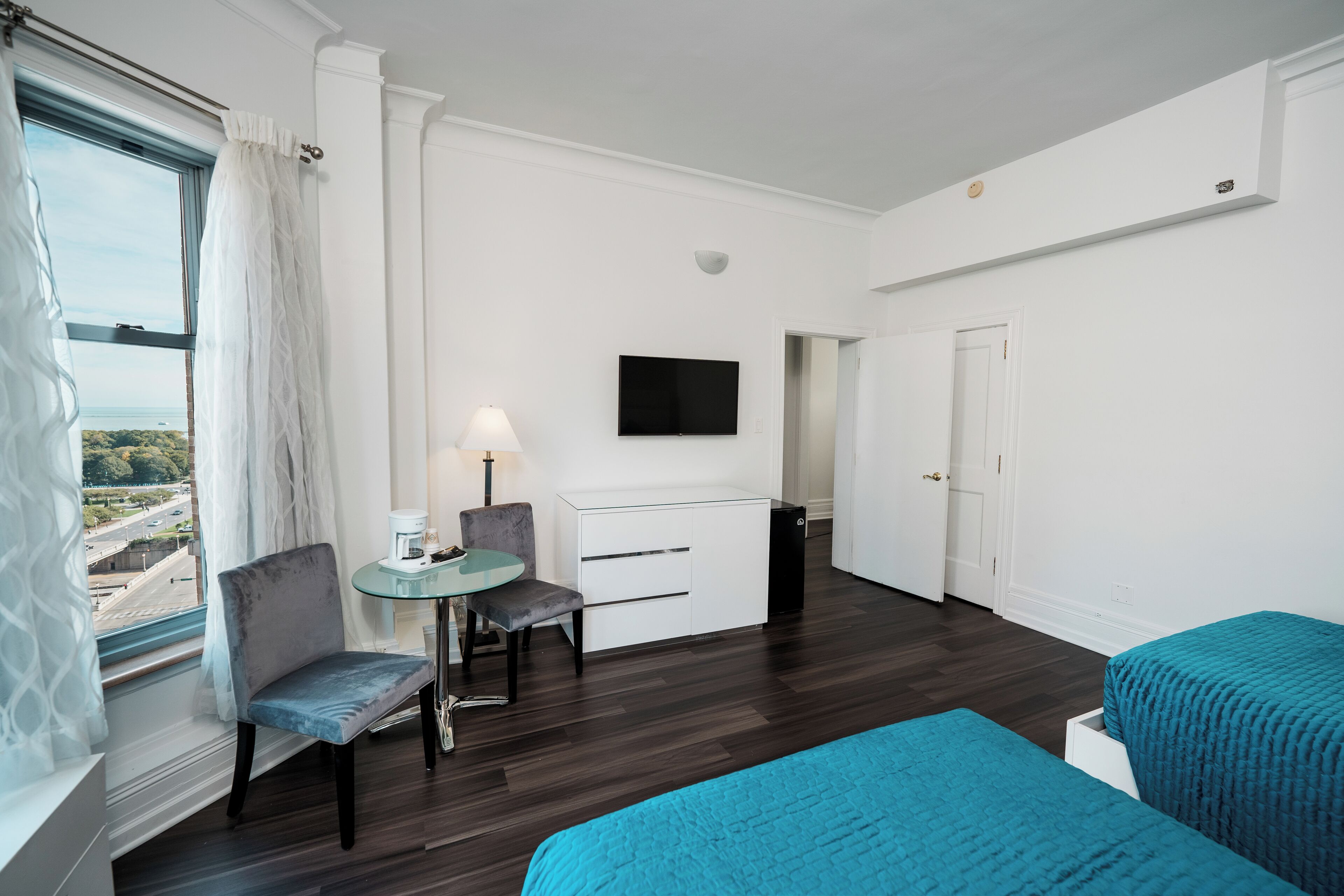 A hotel room with a bed, a desk with a chair, a television, and a window with curtains.