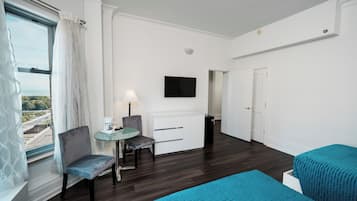 A hotel room with a bed, a desk with a chair, a television, and a window with curtains.
