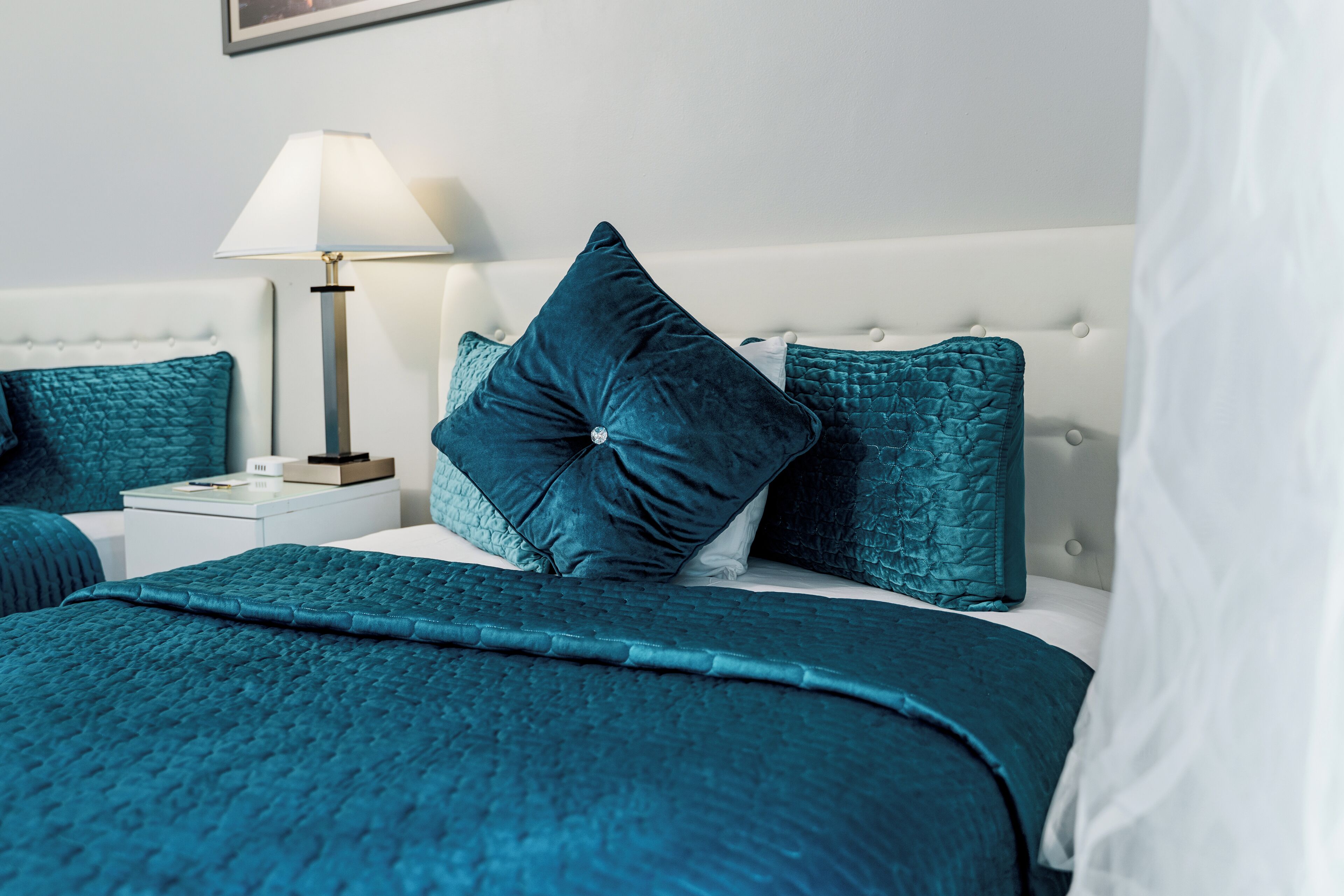 Un letto rifatto con una coperta verde acqua e cuscini, una lampada da comodino e un comodino bianco.
