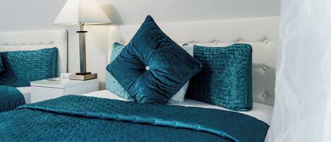 A neatly made bed with a teal bedspread and pillows, a bedside lamp, and a white nightstand.