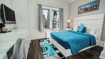 Un dormitorio moderno con vista a la ciudad, una cama grande con ropa de cama azul, un escritorio con computadora y un televisor de pantalla plana.